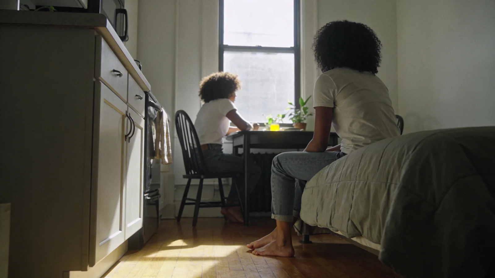 Person sitting on bed edge with bare feet on wooden floor in morning light, body reflecting the challenge of nervous system regulation