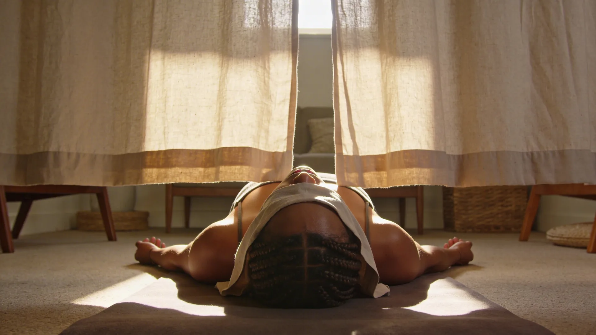 Woman pulling back a heavy curtain in a dim hallway as light streams across her chest and breath