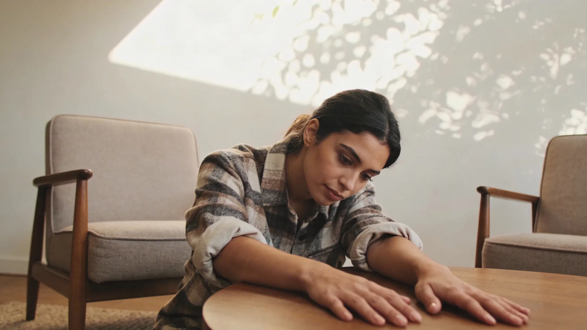Relaxed hands resting palms down beside a ceramic bowl on a wooden table in soft side light