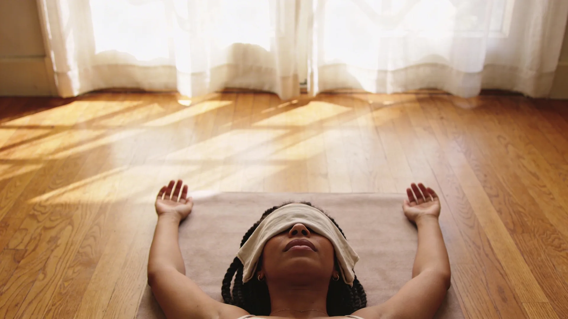 Woman lying in Feeling Session posture on wooden floor with eyes covered, exploring why the burnout recovery timeline feels confusing