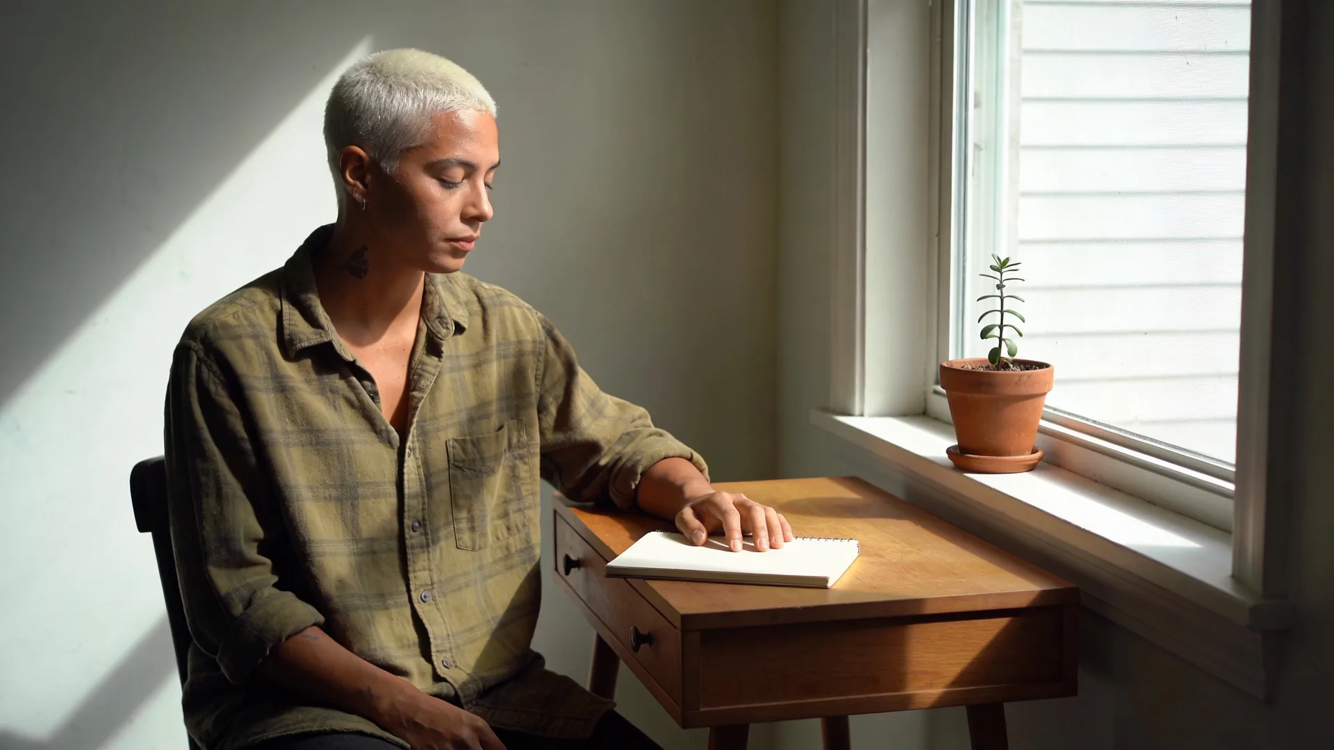 Feeling empty — seated at a small writing desk by a window, hand resting on a closed notebook
