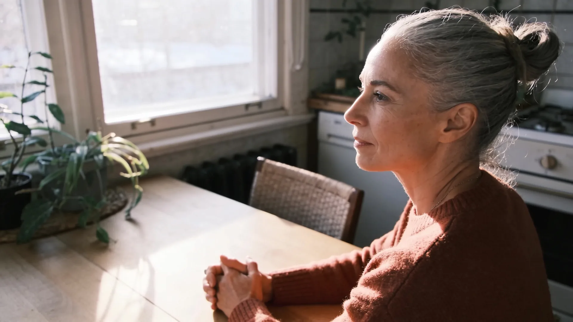 Two people sitting quietly at a kitchen table sharing stillness, tenderness without performance
