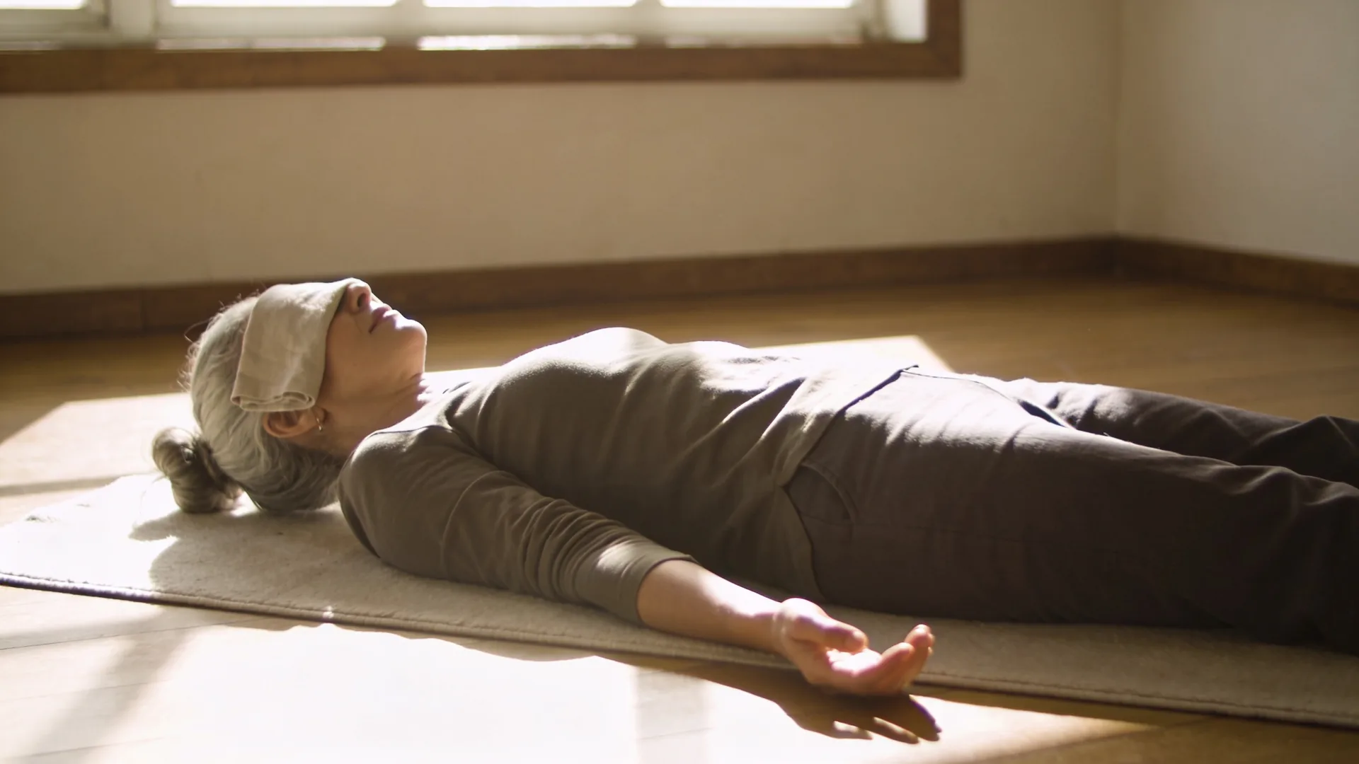 Woman standing near open window with relaxed body as curtain billows, fear easing toward safety in the body