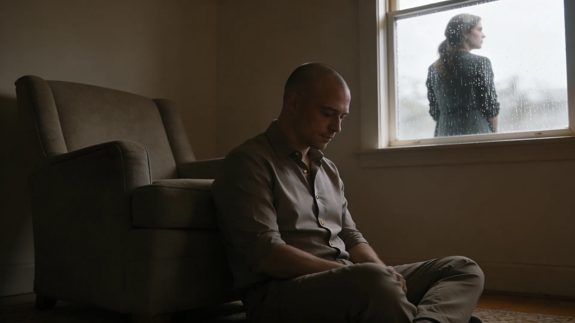 Man standing at rain-streaked window in a quiet living room contemplating how long does grief last