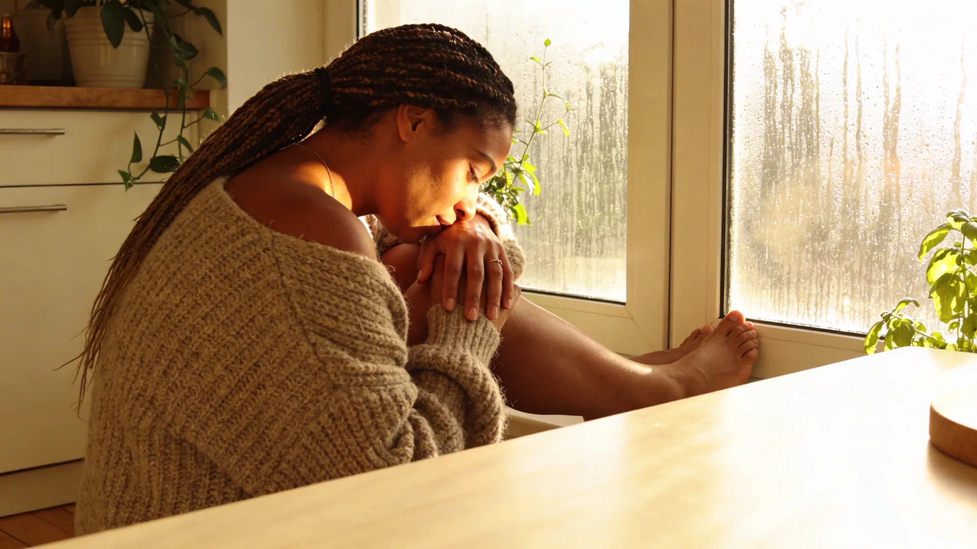 Woman leaning forehead against rain-streaked window from behind, stillness expressing the struggle of how to let go of control