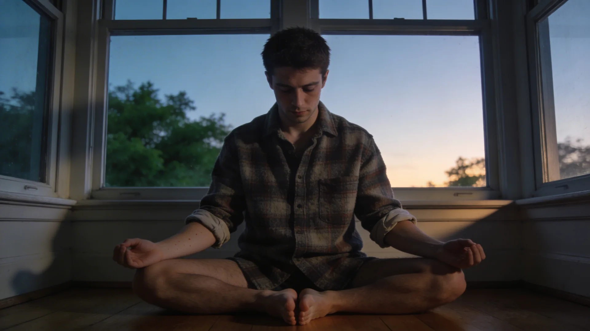 Man sitting on bed edge with bare feet on wooden floor practicing nervous system regulation exercises in morning light