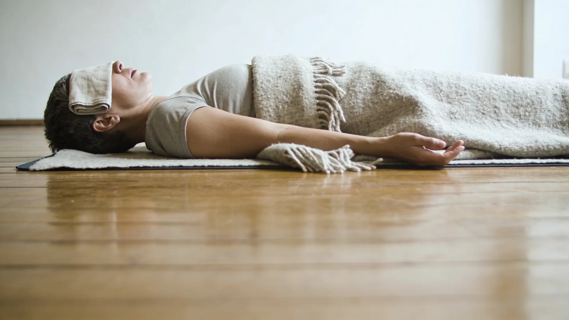 Body under a heavy wool blanket on a wooden floor showing freeze response easing toward safety