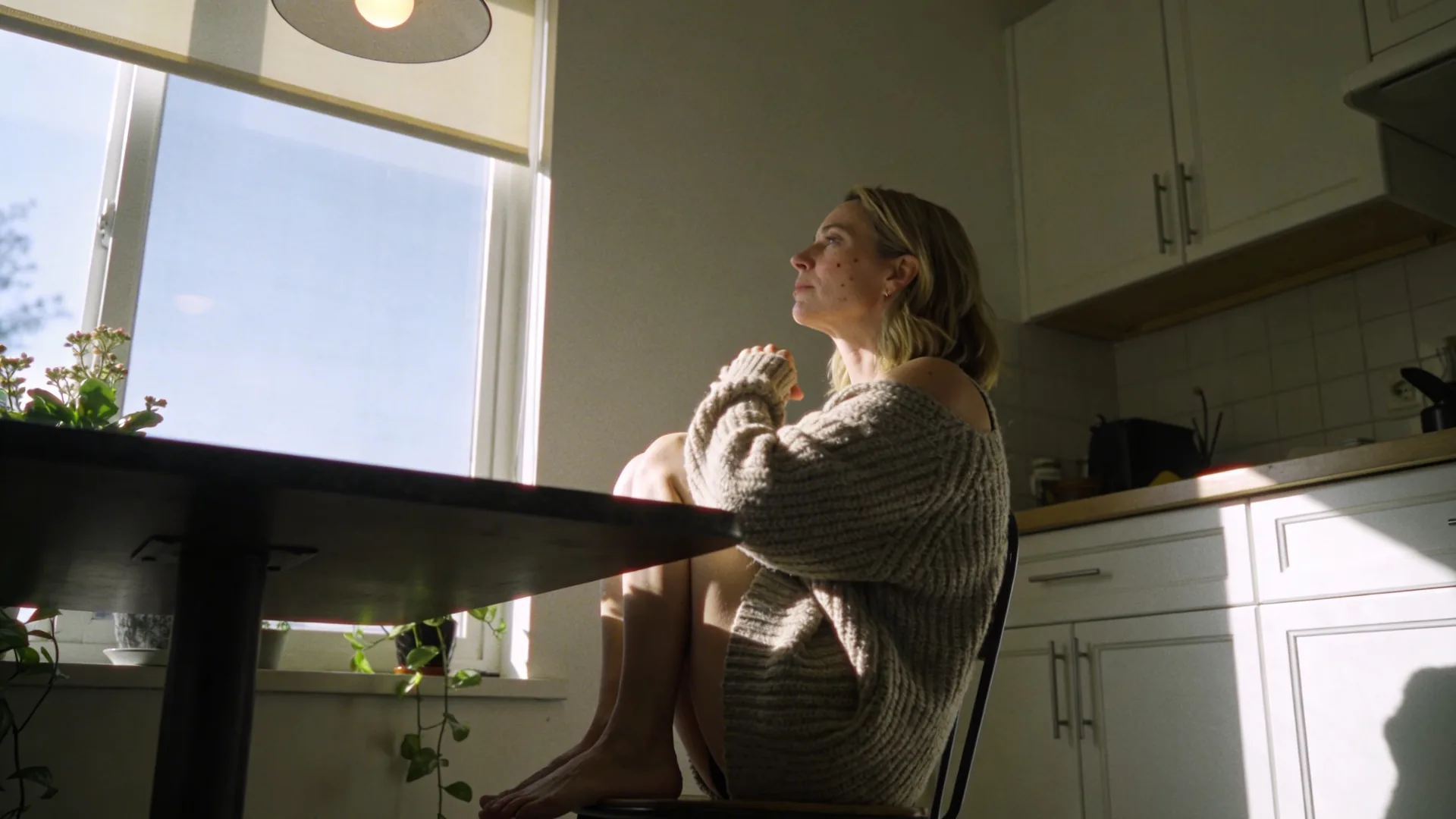 Woman pausing at a sunlit desk during a spiritual crisis, body tense with shoulders raised