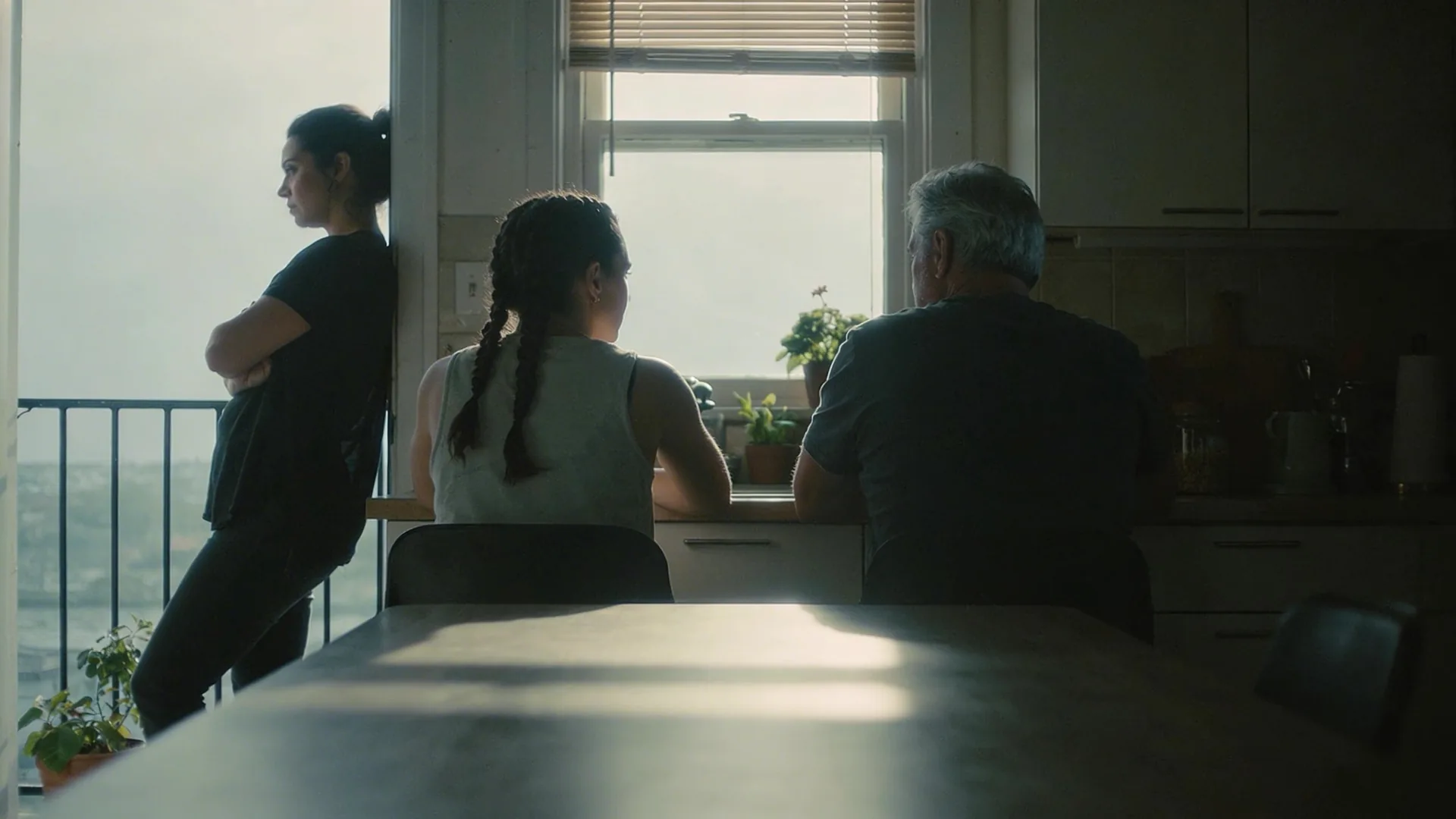 Woman leaning against a balcony doorframe in a dim kitchen showing why grief gets stuck even when trying everything