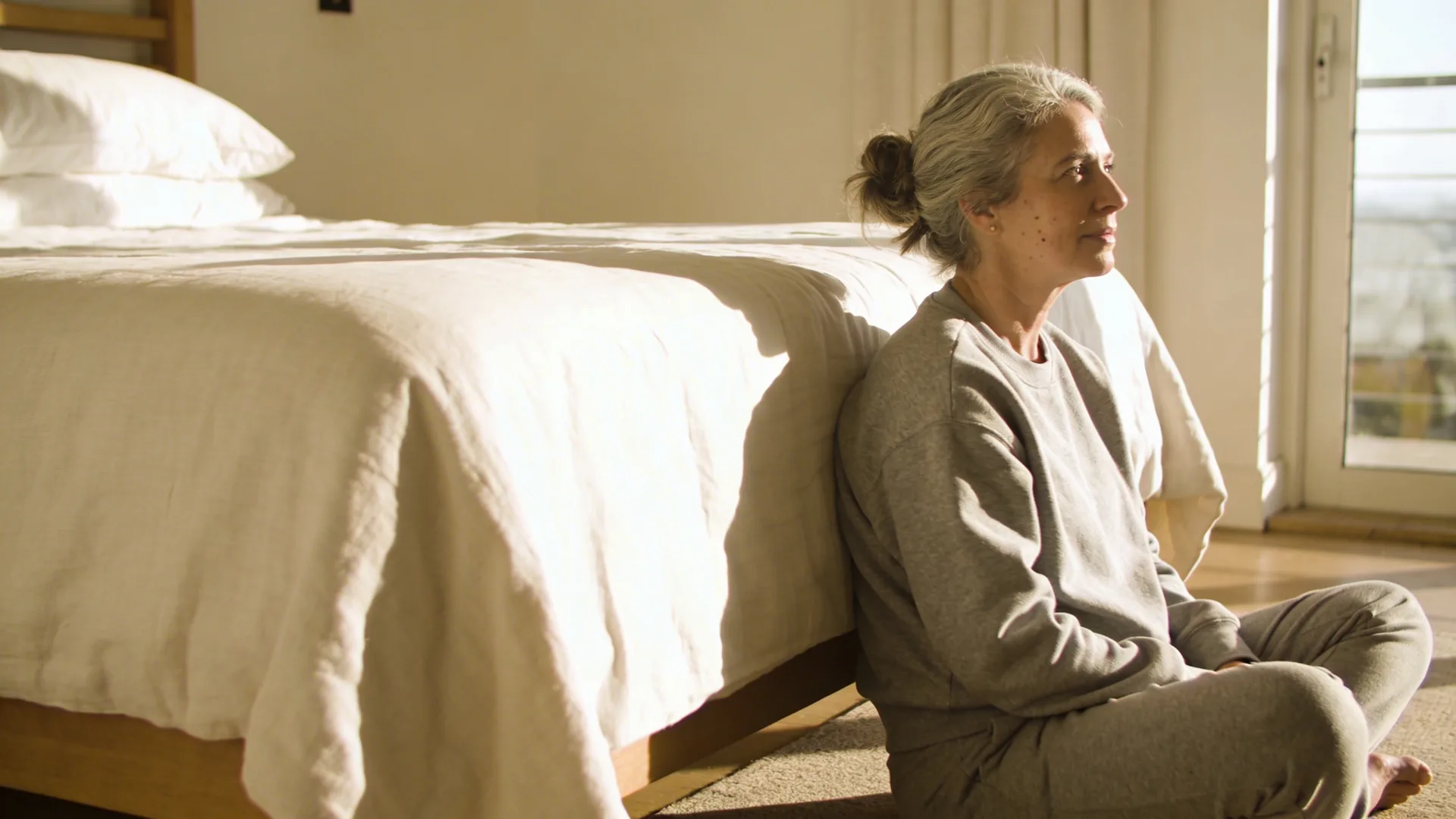 Woman seated on floor beside bed at night beginning a 12-minute self compassion reset