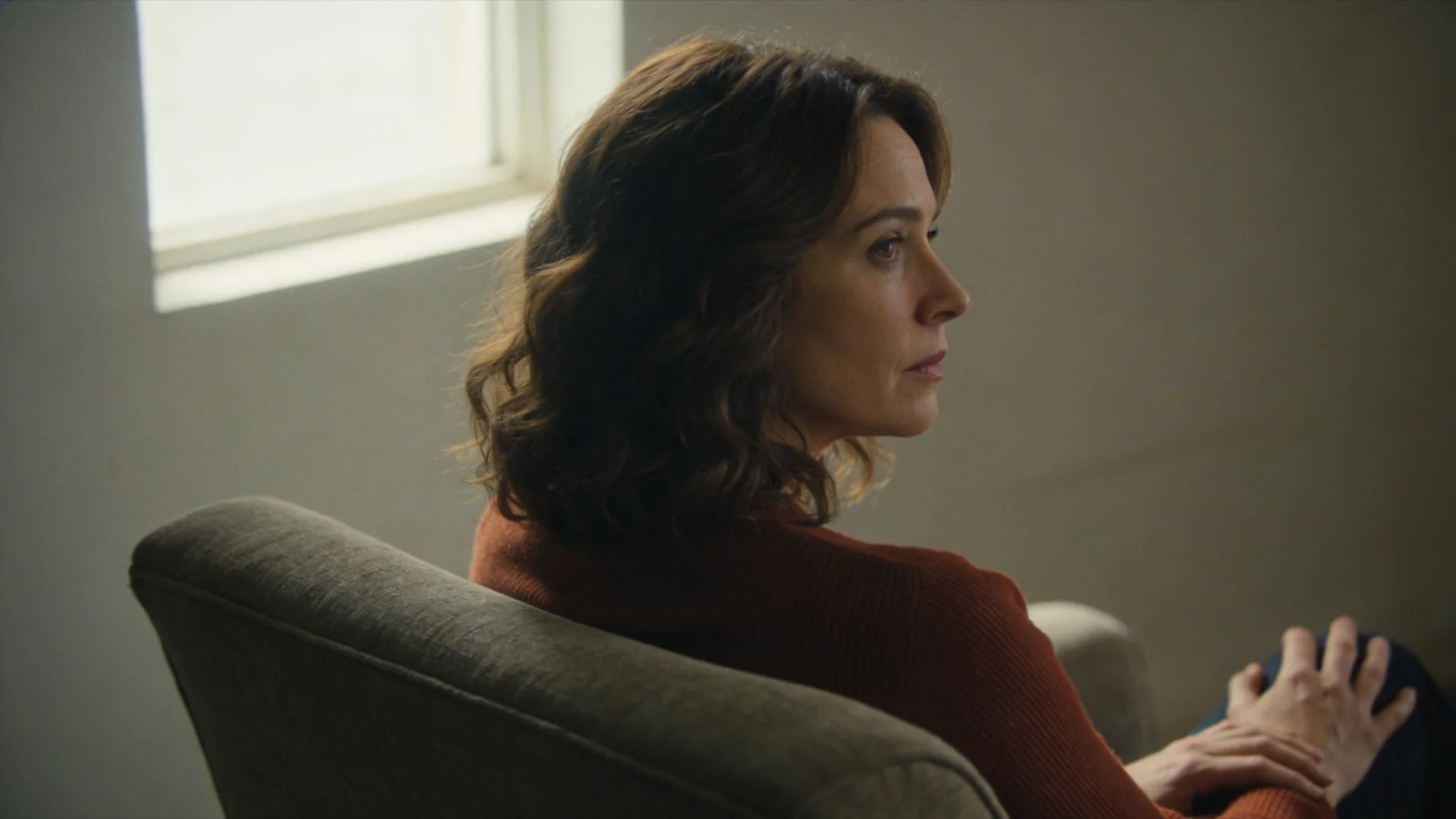 Woman sitting at desk at night wondering why cant i open up to anyone, arms crossed over chest near rain-streaked window
