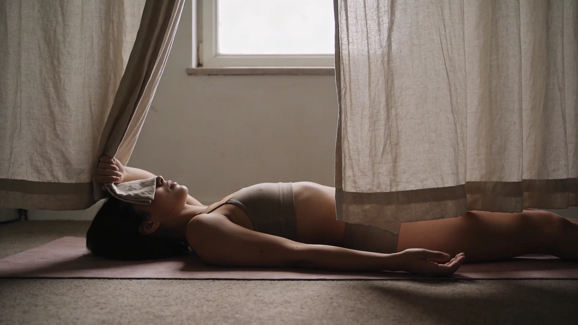 Woman pulling back curtain in dim hallway, body caught in soft light, where emptiness lives in the body