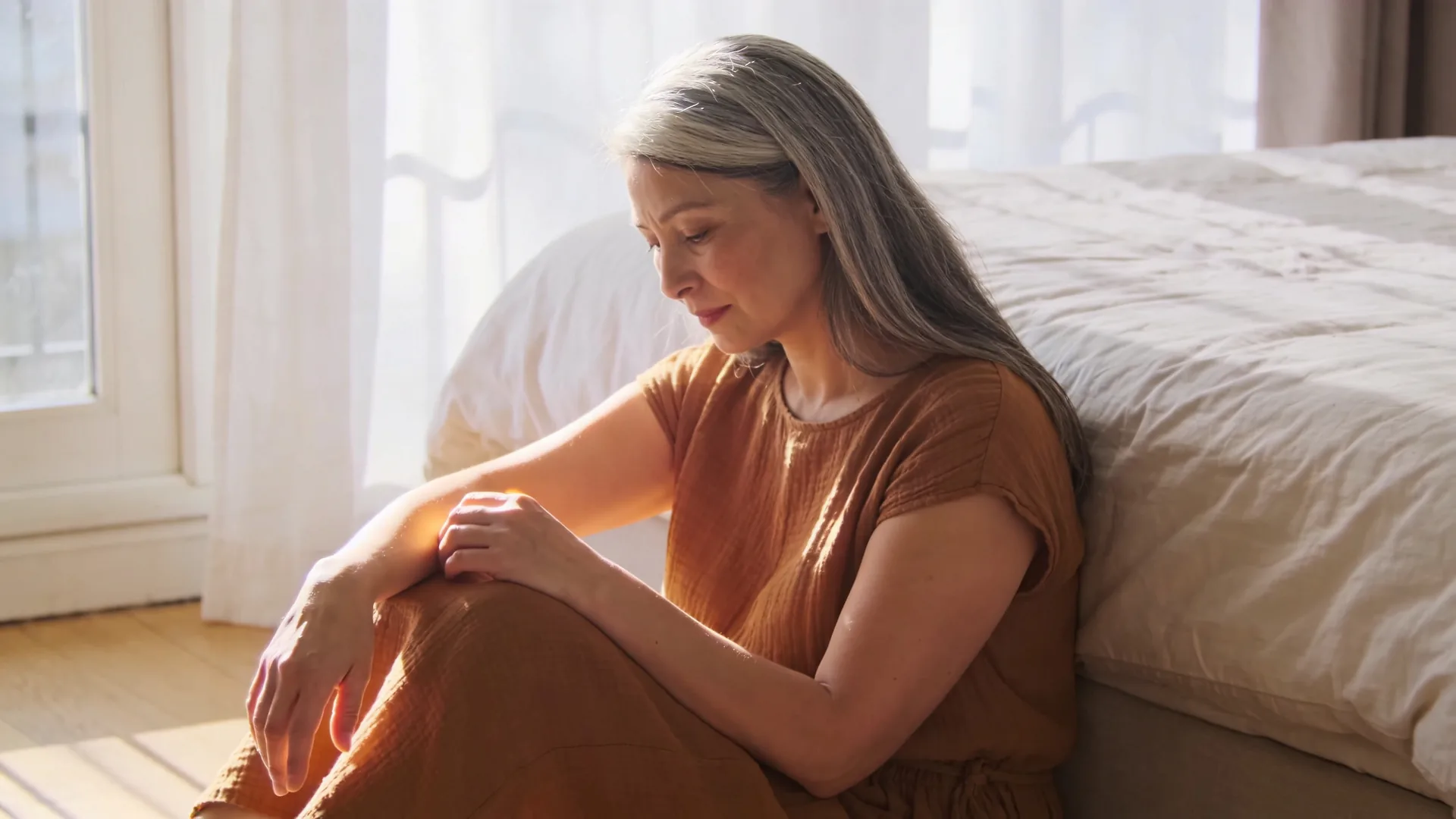 Woman sitting on wooden floor in dim lamplight, gaze turned inward, capturing what overthinking actually is in quiet stillness