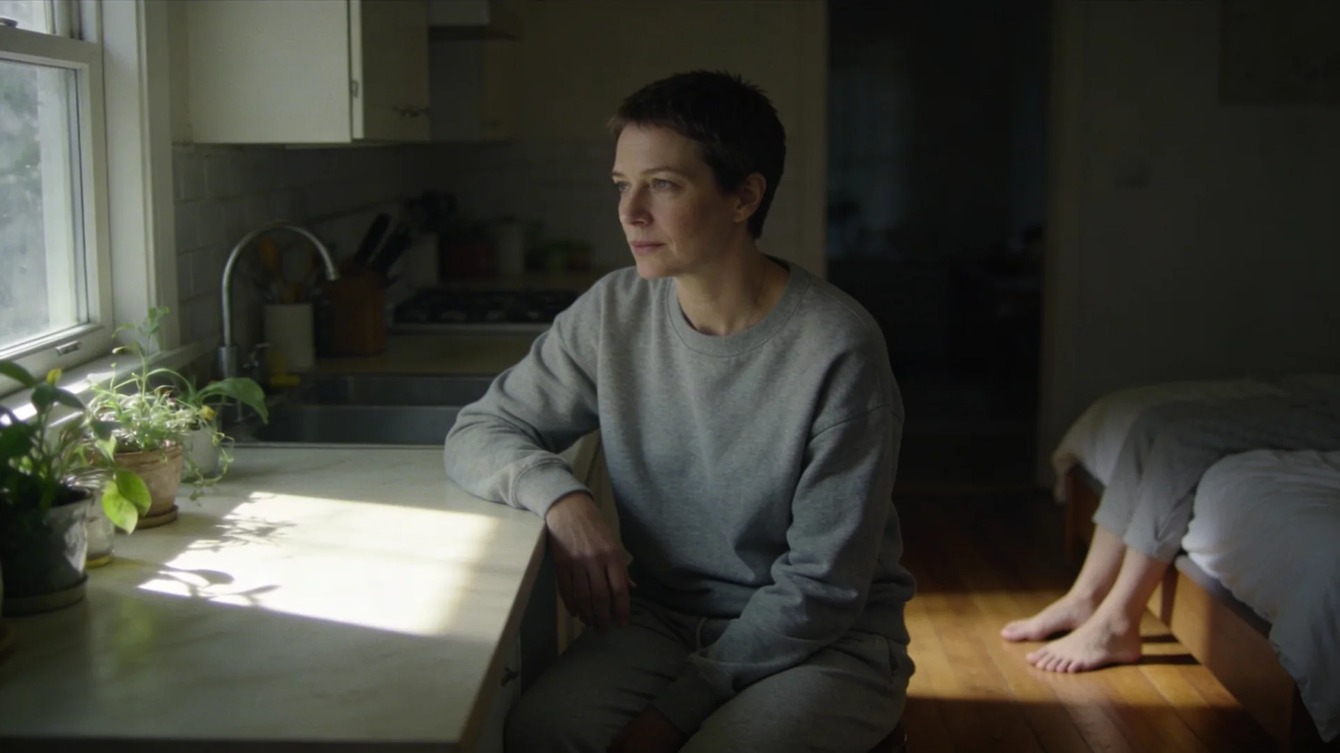 Woman sitting on bed edge with bare feet on wooden floor in dim morning light, showing why do I shut down emotionally